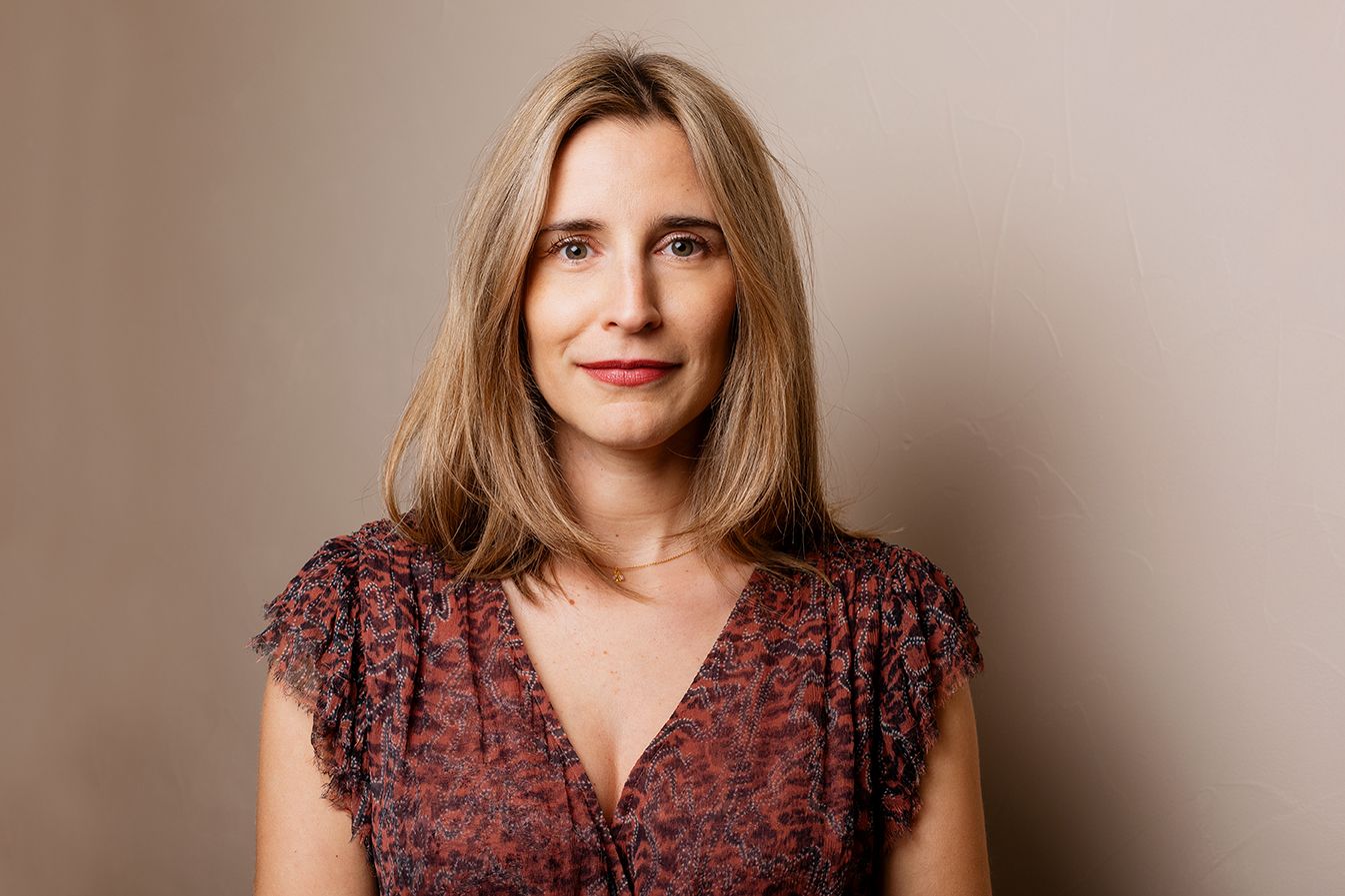 Blonde woman in floral top posing against neutral beige background in professional portrait.
