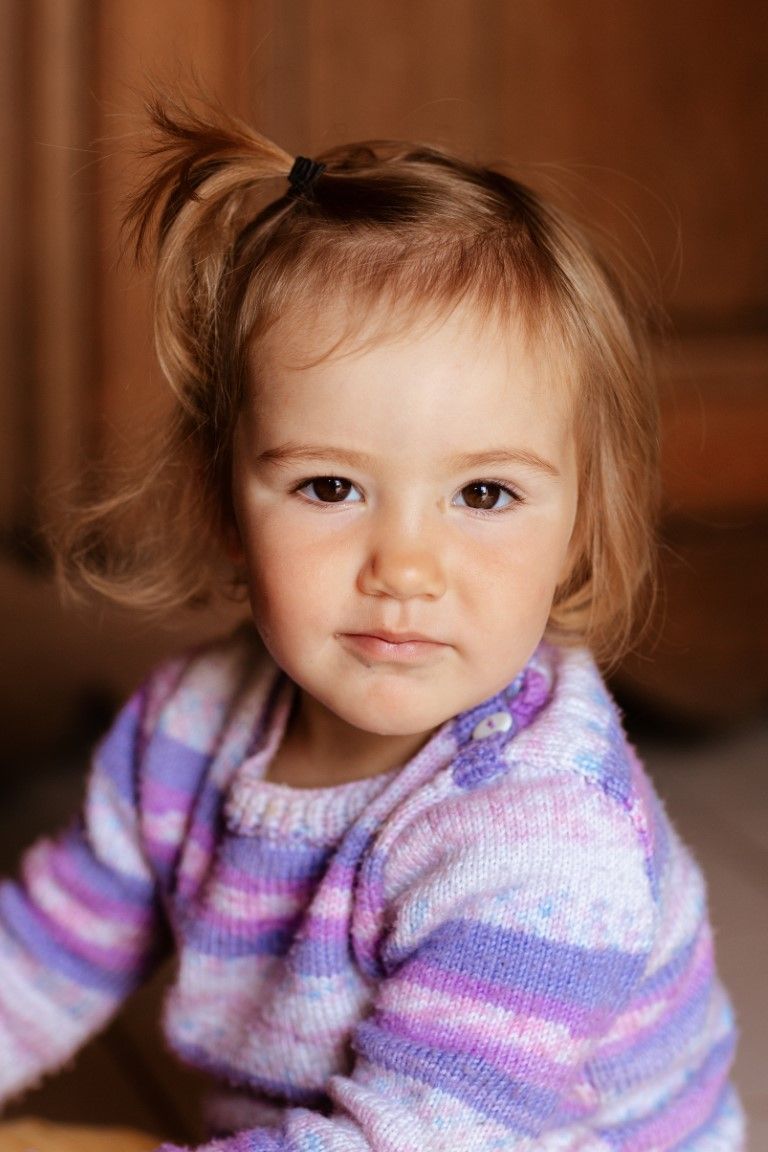 Portrait en gros plan d'une adorable petite fille avec une petite queue de cheval, portant un pull en maille, à l'intérieur