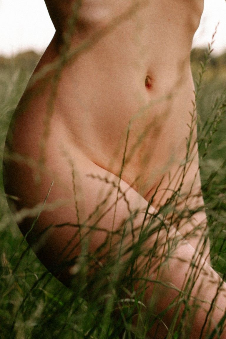 A person's bare torso and legs sitting in tall green grass in a natural outdoor setting.