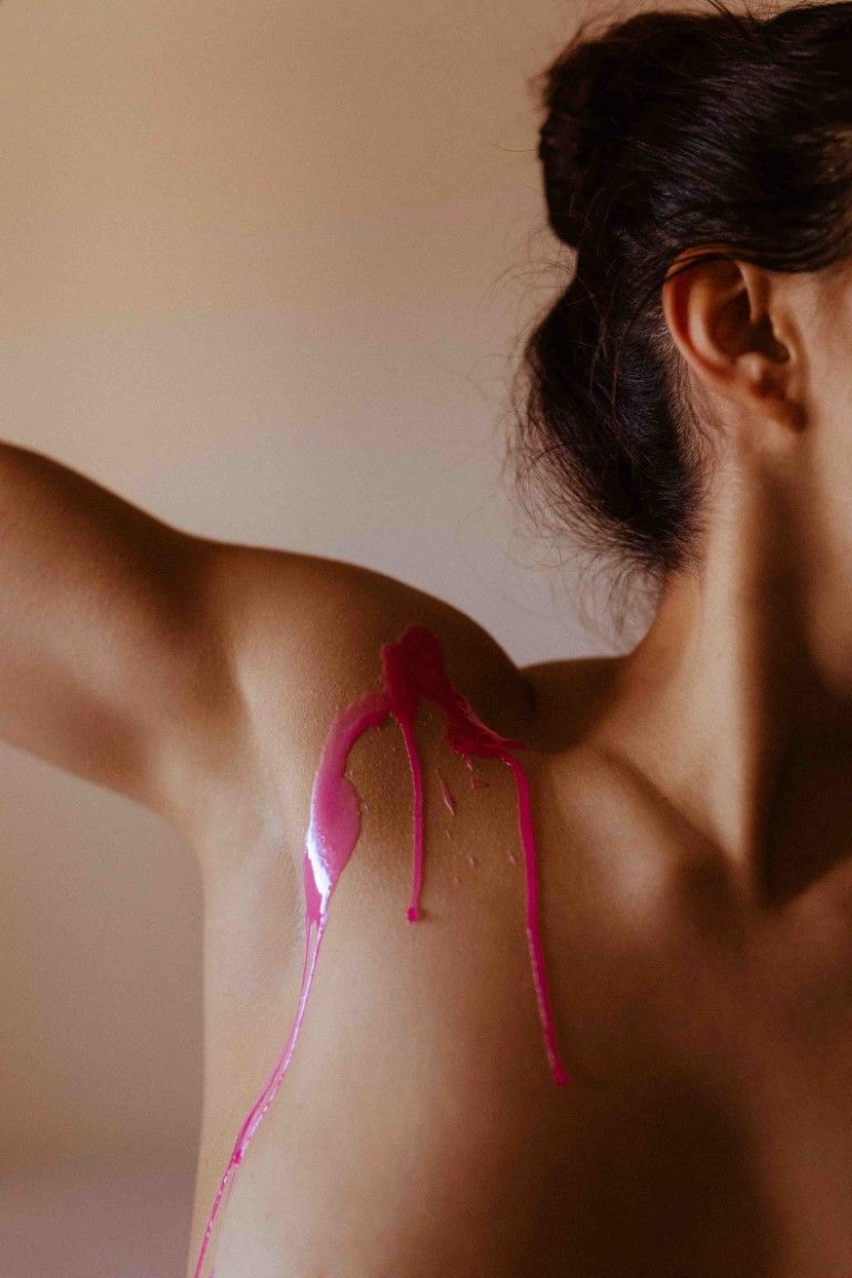 Close-up artistic photo of pink paint dripping down a bare shoulder and upper back.