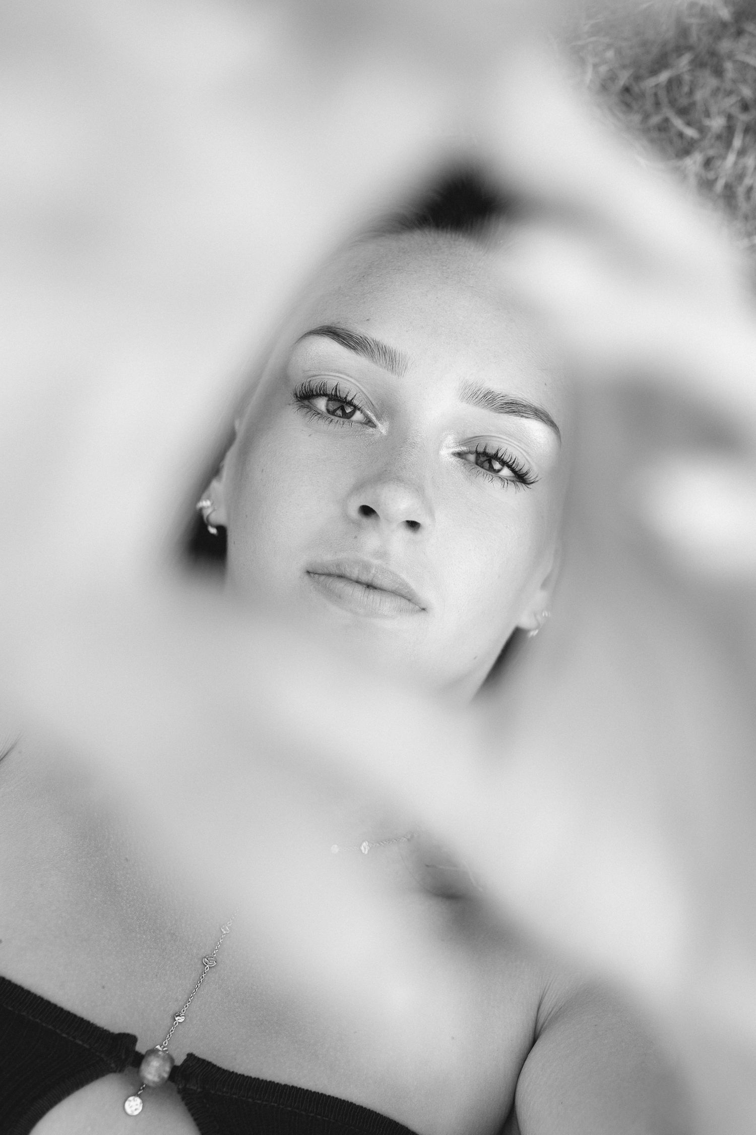 Portrait artistique en noir et blanc d'une jeune femme blonde, les mains encadrant son visage et un bracelet visible.