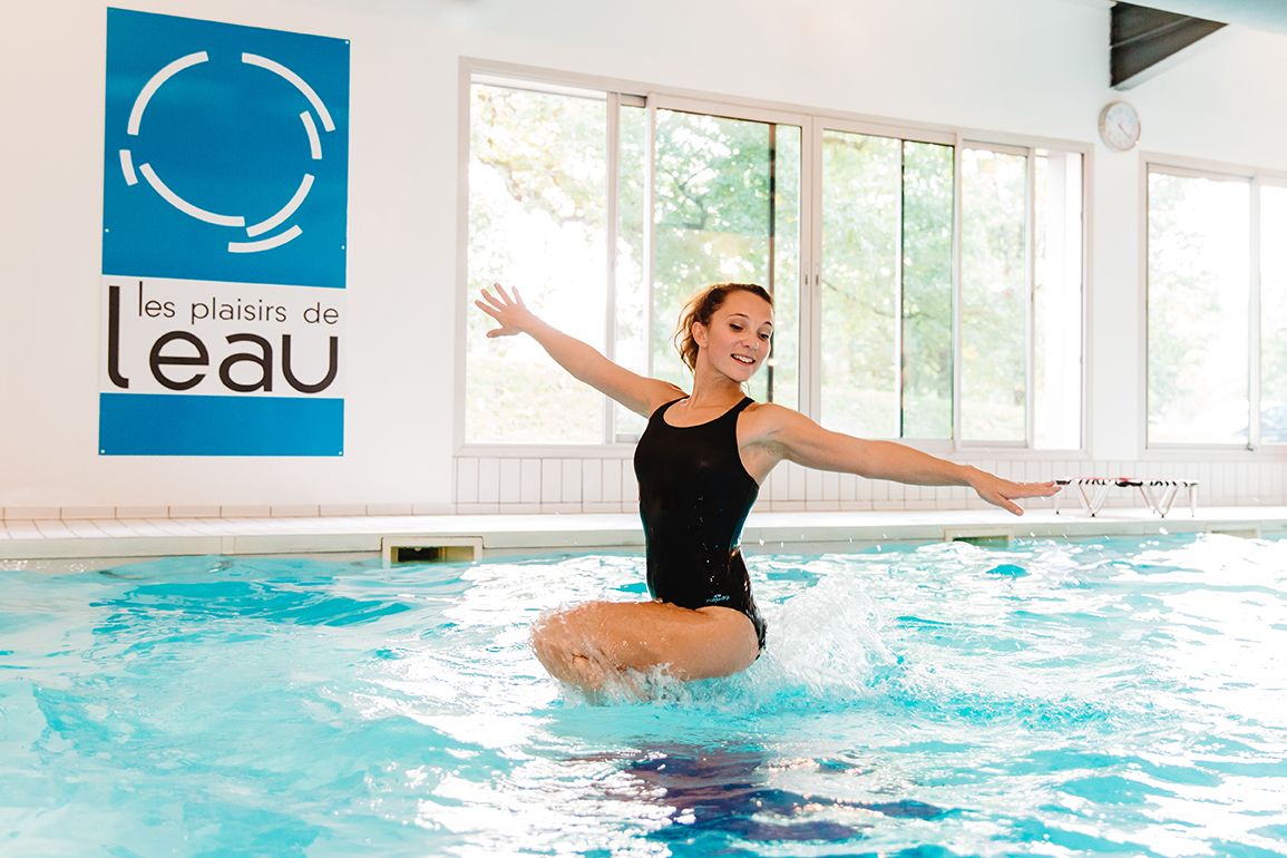 Woman jumping joyfully in an indoor swimming pool at Les Plaisirs de l eau facility.