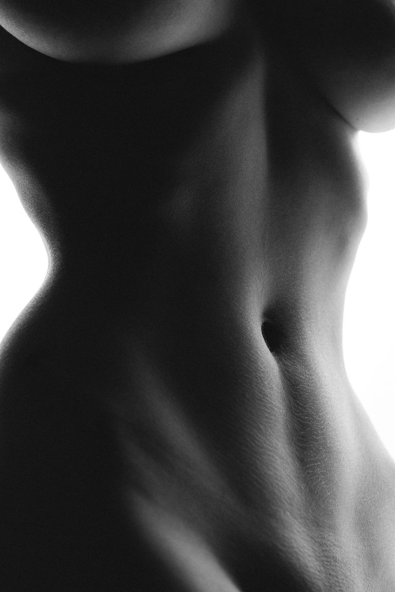Photo en noir et blanc à contraste élevé d'un nu féminin, représentant un torse et une taille de femme musclée sur fond de lumière
