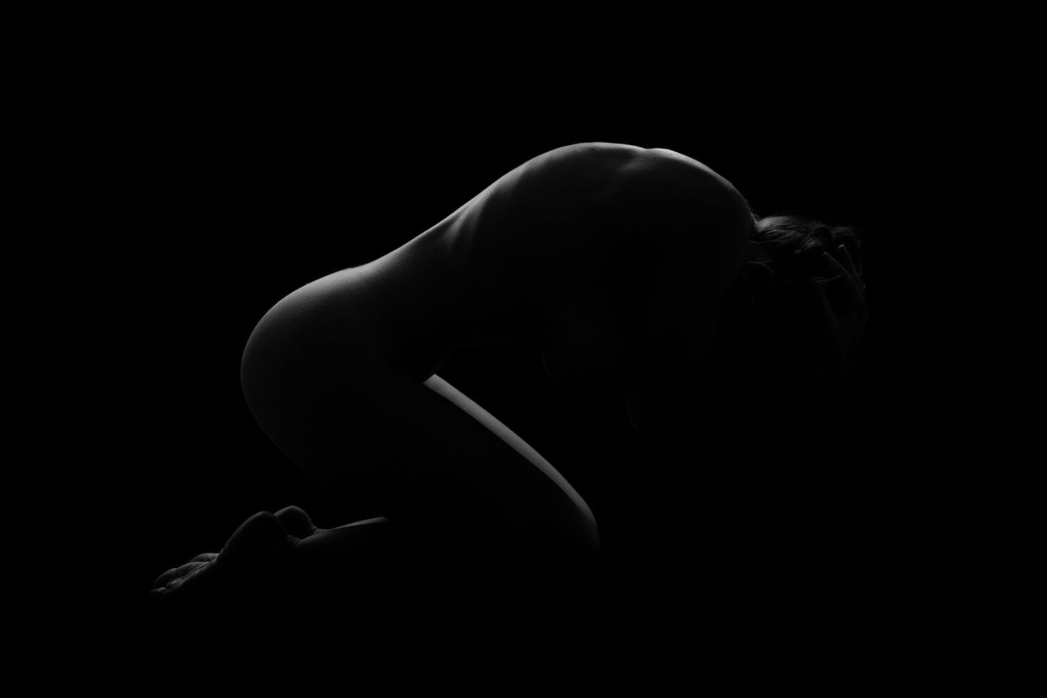 Artistic black and white silhouette of a nude figure curled in shadow, dramatic low-key lighting photography.