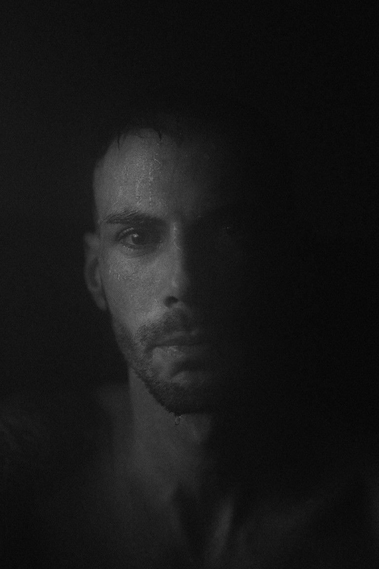 Portrait en noir et blanc, d'une sobriété saisissante, d'un homme barbu émergeant des ténèbres.