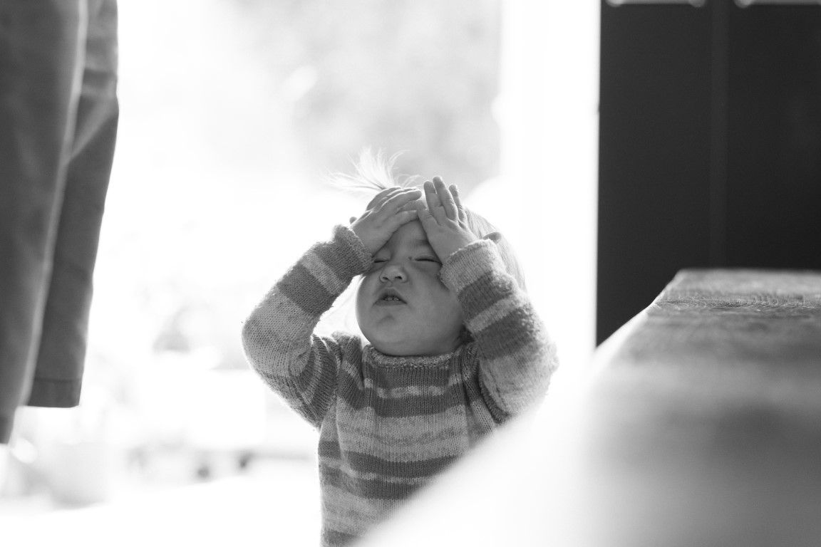 Photo en noir et blanc d'un tout-petit en pull rayé, levant les mains vers le ciel, l'air émerveillé.