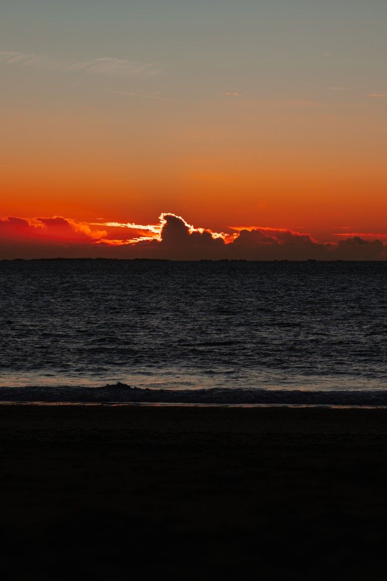 Coucher de soleil aux teintes rouge orangé profond sur les eaux calmes de l'océan, avec des nuages ​​en silhouette en basse Normandie
