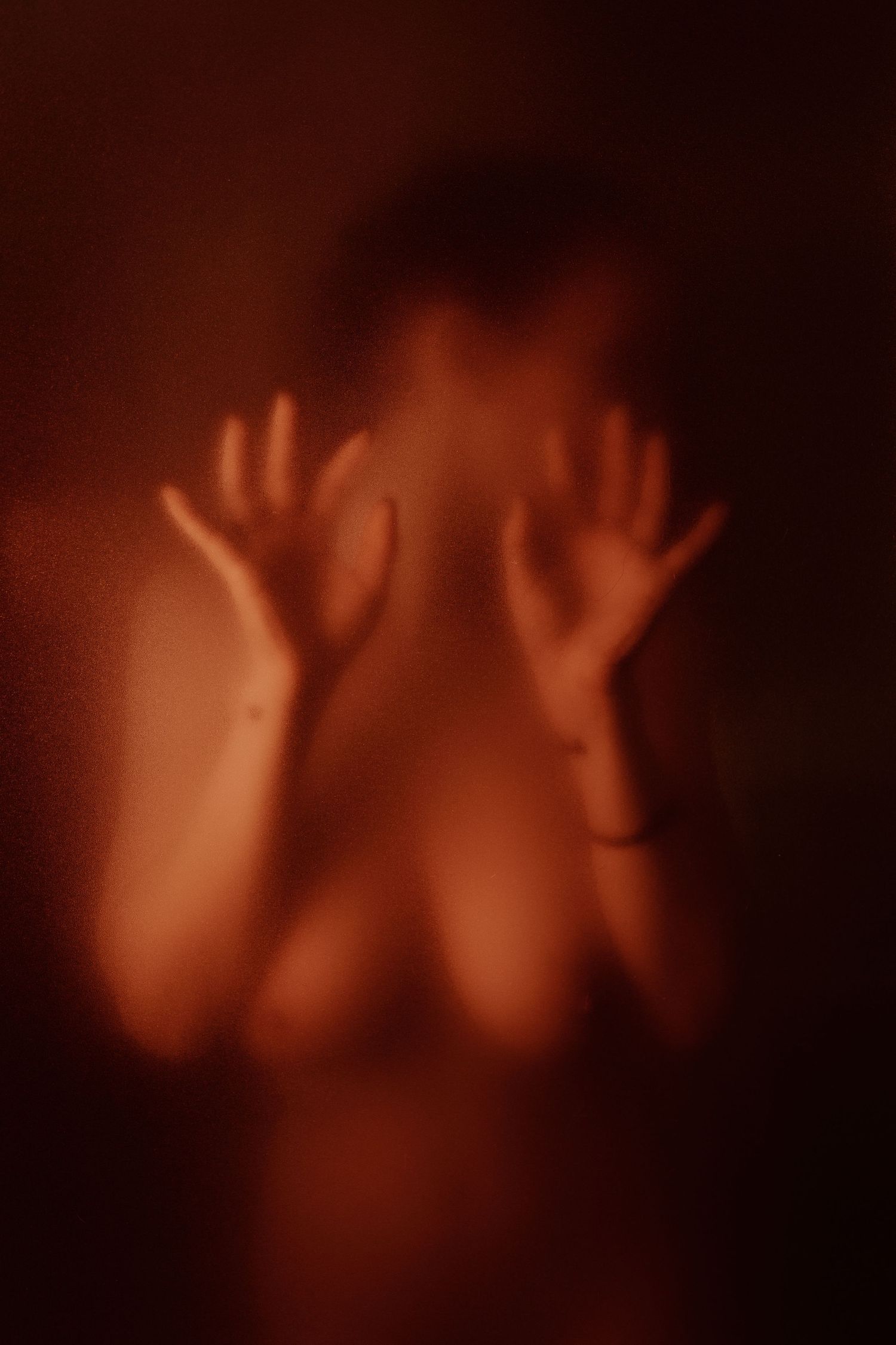 Silhouette of a person pressing hands against frosted glass in dramatic red lighting.