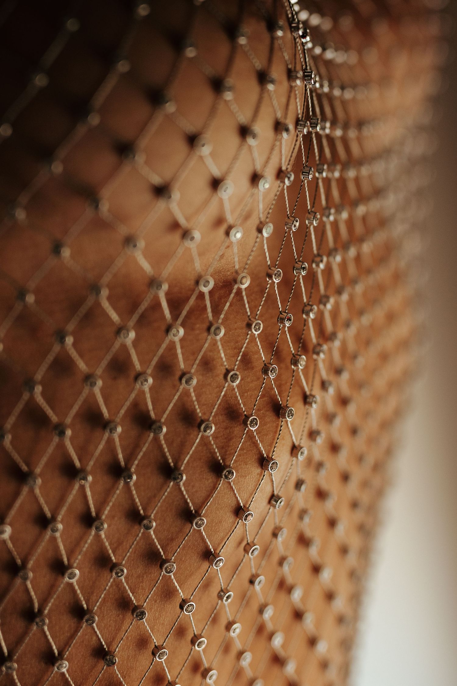 Close-up of a tufted brown velvet headboard with diamond pattern and decorative silver button details.
