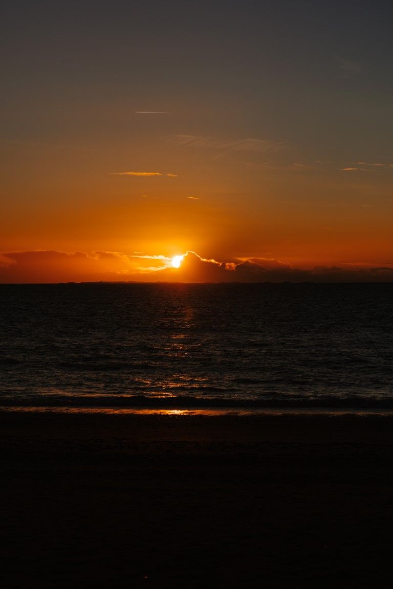 Un coucher de soleil orange éclatant sur l'océan, avec des nuages ​​spectaculaires à l'horizon au crépuscule.