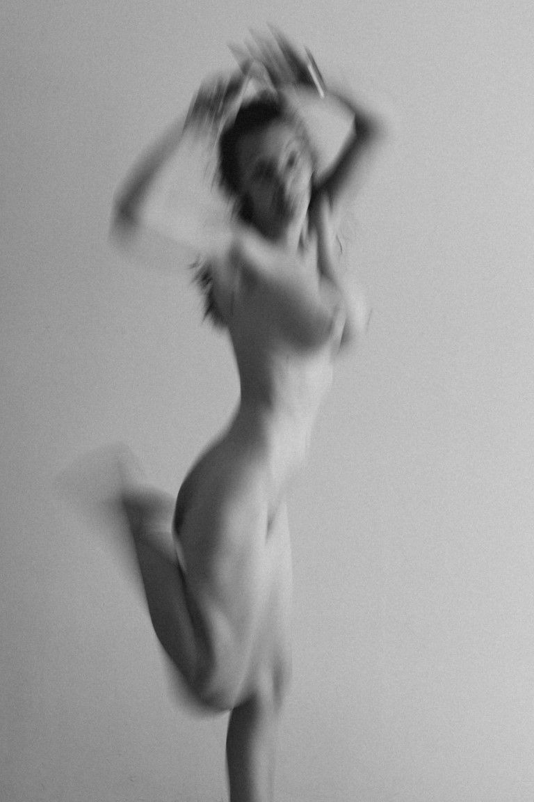 Nu artistique flou en noir et blanc d'une femme dansant les bras levés en studio.
