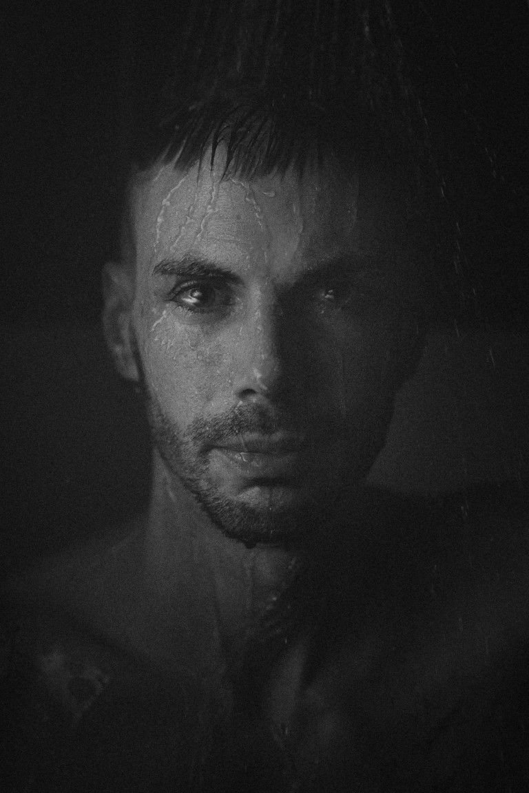 Portrait en noir et blanc, sombre et mélancolique, d'un homme aux cheveux mouillés et au regard intense.