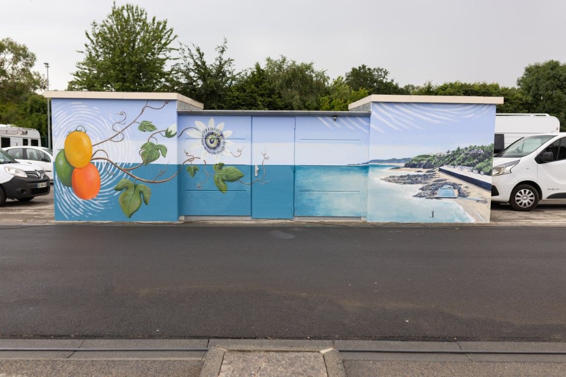 Colorful coastal mural painted on a utility building in a parking lot, featuring ocean scenery and tropical fruit artwork.