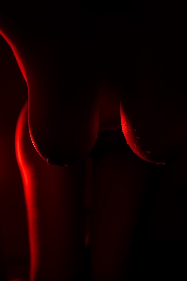 Silhouette artistique éclairée en rouge des courbes d'une femme sur fond noir.