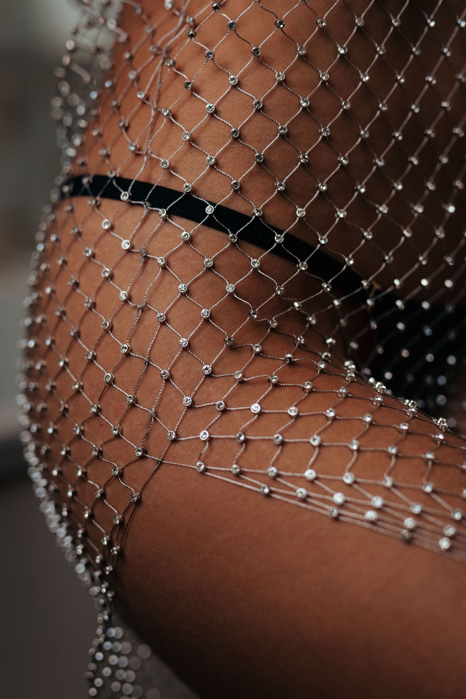 Close-up of a sparkling rhinestone mesh net overlay on dark skin, featuring crystal embellishments in a diamond pattern.