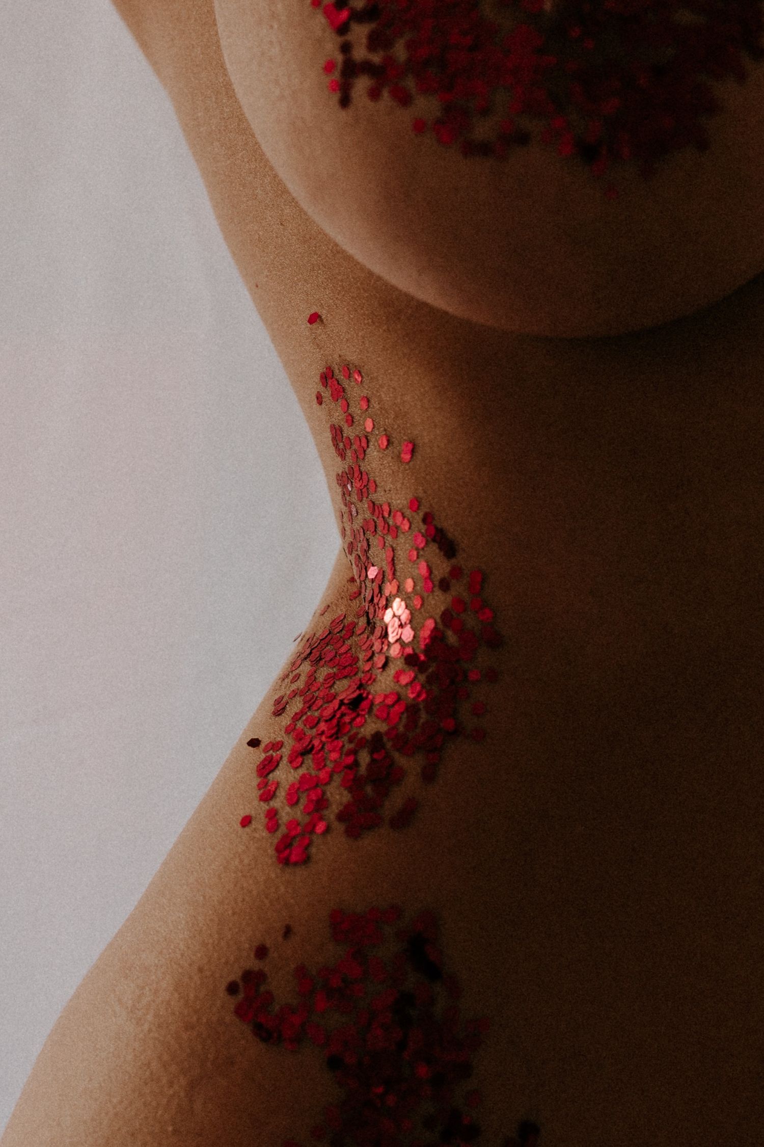 Close-up of a human torso adorned with scattered red sequins against smooth skin on a neutral background.