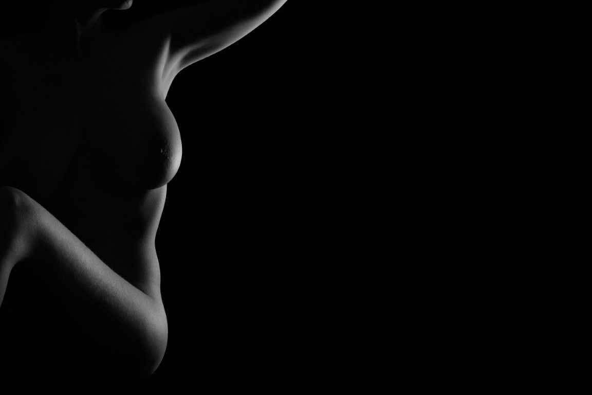 Black and white artistic silhouette photograph of a female figure against a dark background.