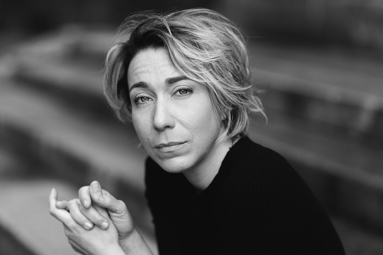 Portrait en noir et blanc d'une femme pensive aux cheveux blonds courts, les mains jointes.