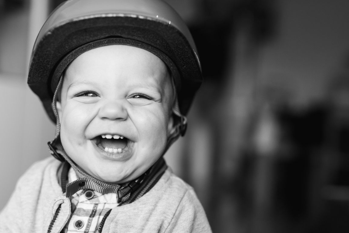 Un tout-petit riant aux éclats, portant un casque, sur une photo portrait en noir et blanc.