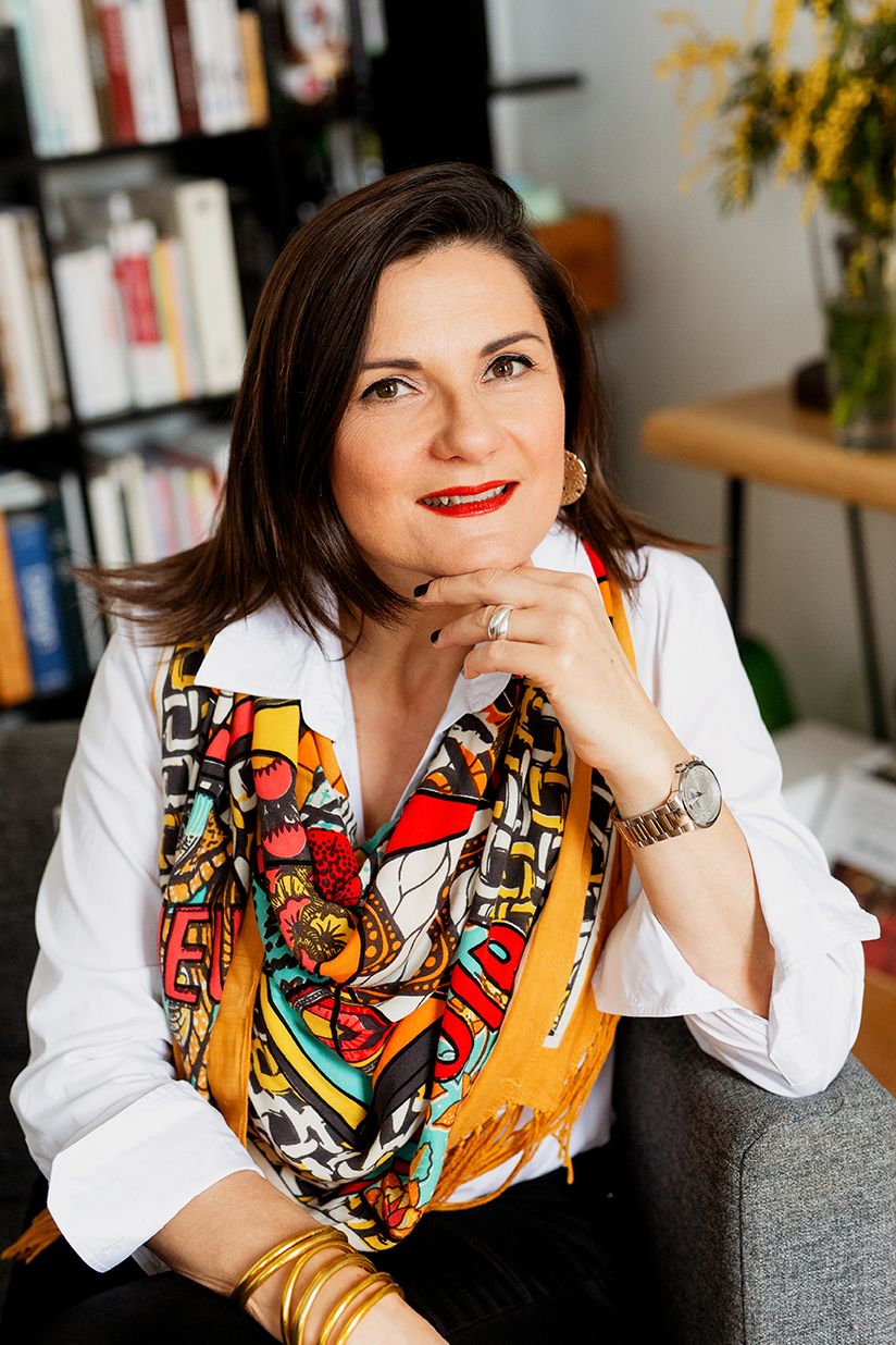 Elegant woman in white shirt and colorful scarf sitting in home library setting.