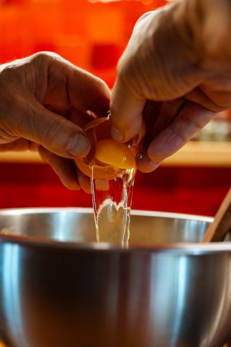 Hands cracking a fresh egg into a stainless steel mixing bowl for baking.