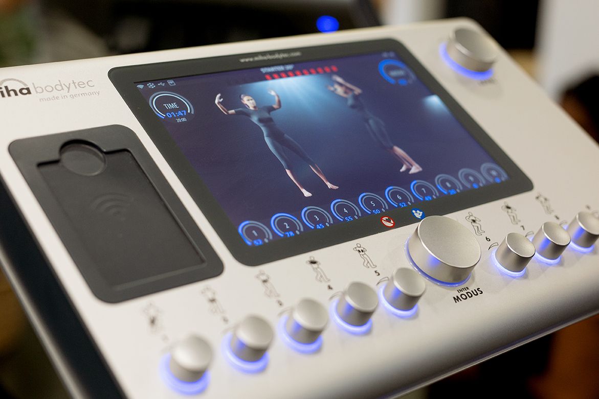 Miha Bodytec EMS training device with touchscreen display showing body silhouette and control knobs.