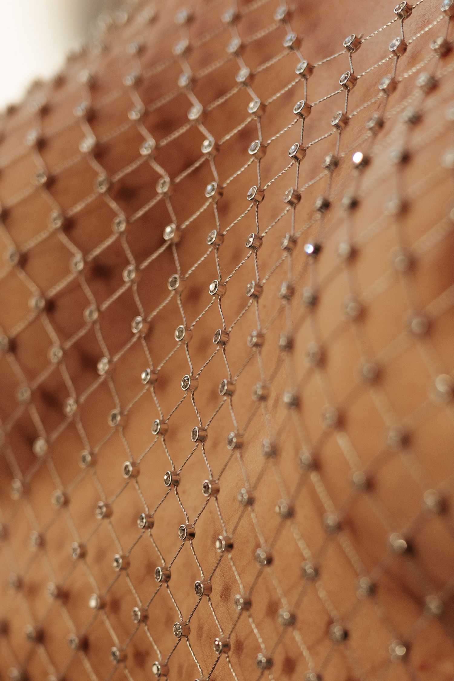 Close-up of sparkling rhinestone fishnet fabric with diamond-pattern mesh and crystal embellishments on skin.