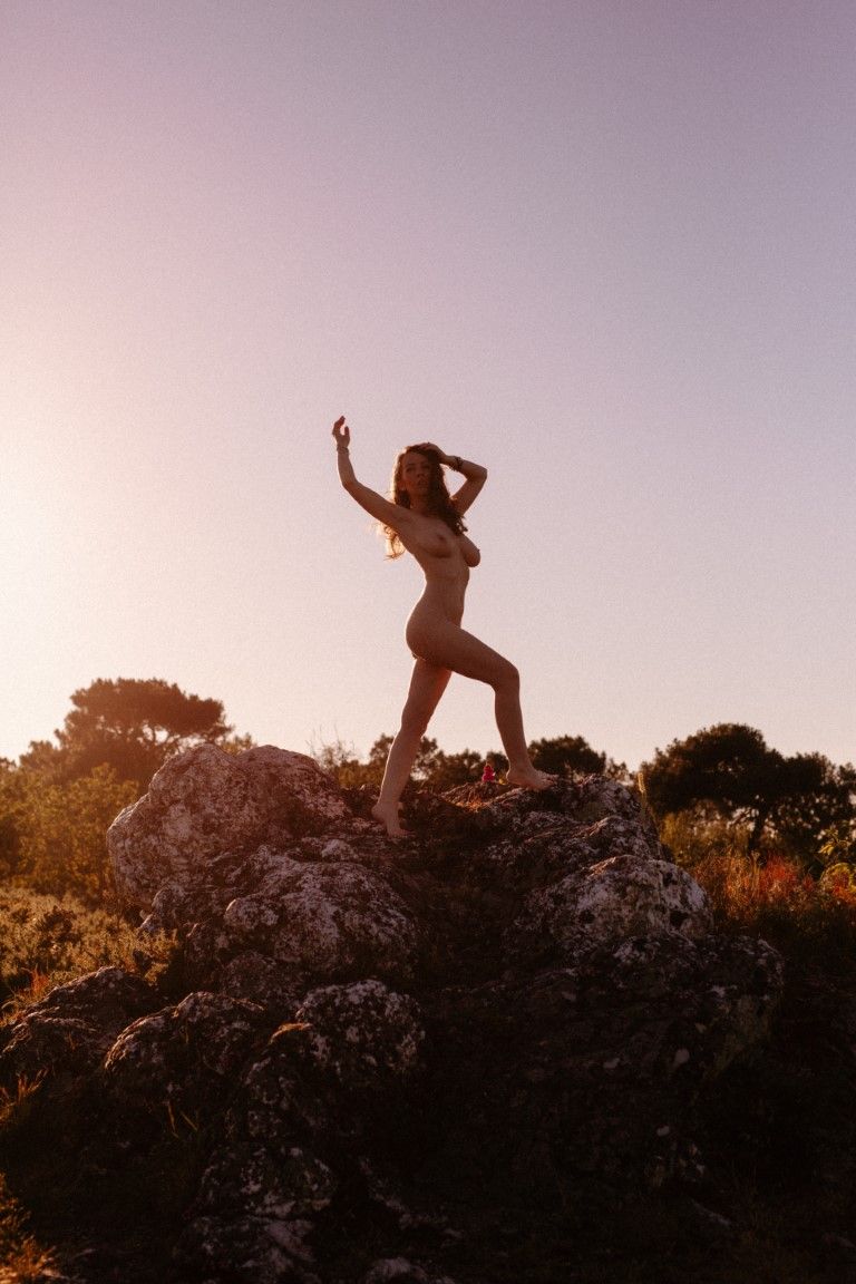 Silhouette of a woman posing on rocky terrain at golden sunset with trees in background.