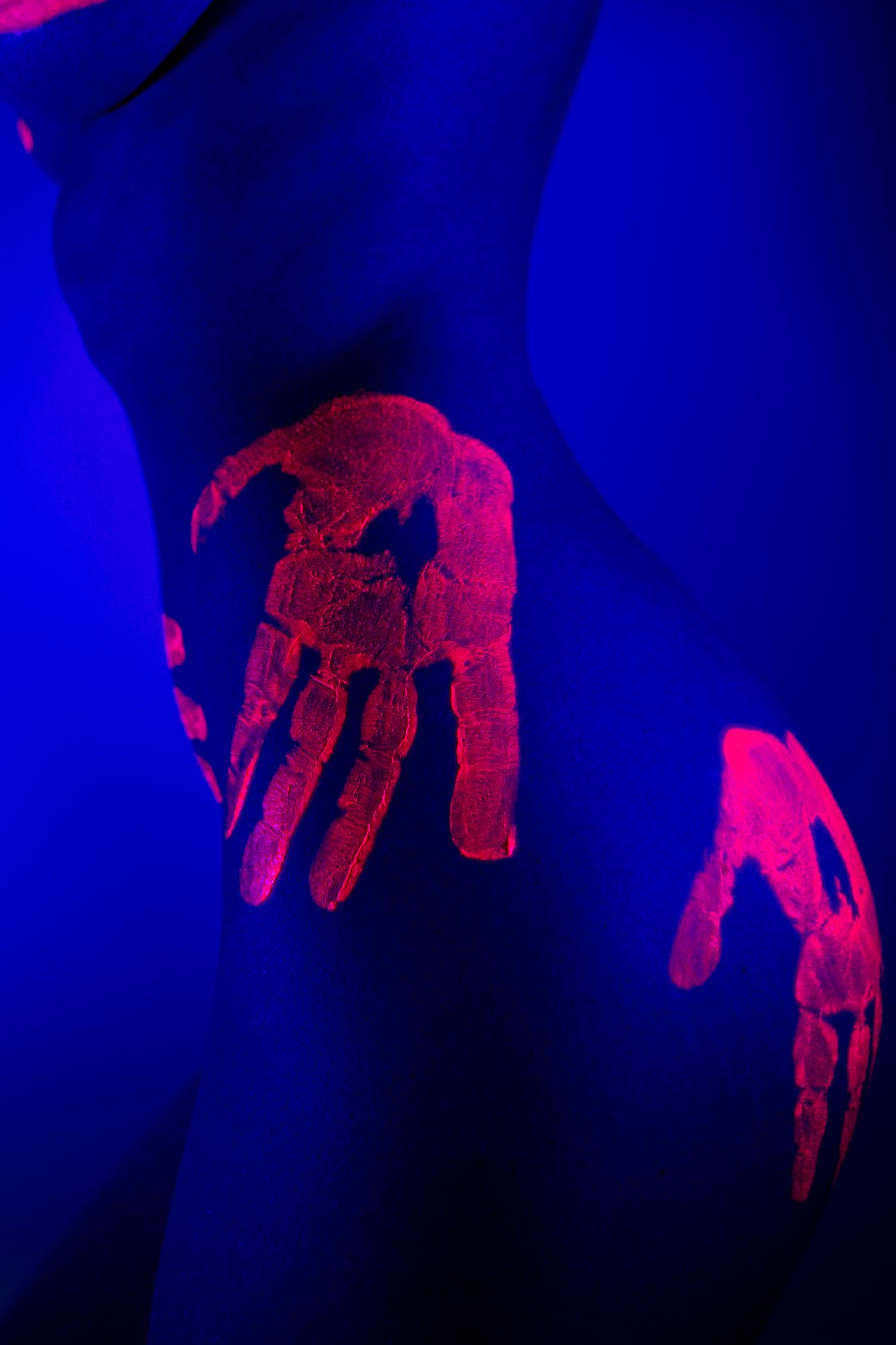 Empreintes de mains fluorescentes rougeoyantes sous lumière UV sur un buste féminin, capturées par photographie à la lumière noire ultra