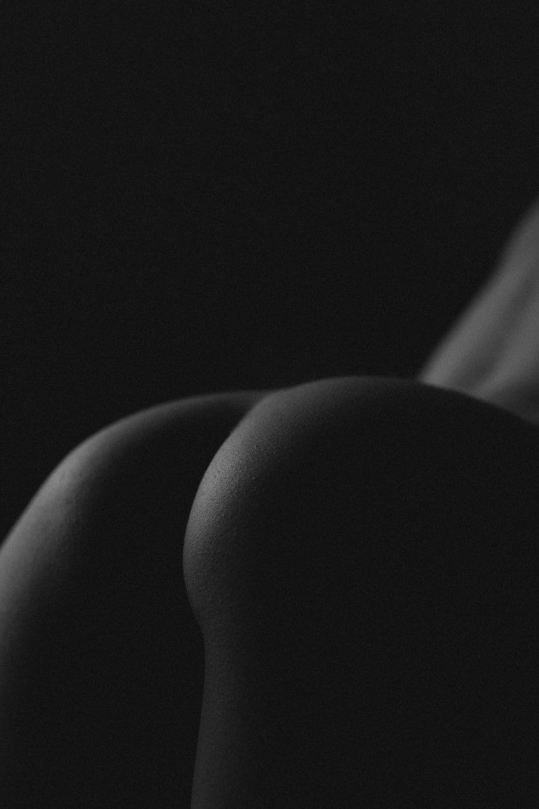 Photo de nu artistique en noir et blanc avec une lumière en clair obscur sur les courbes des fesses d'une femme vue de dos.