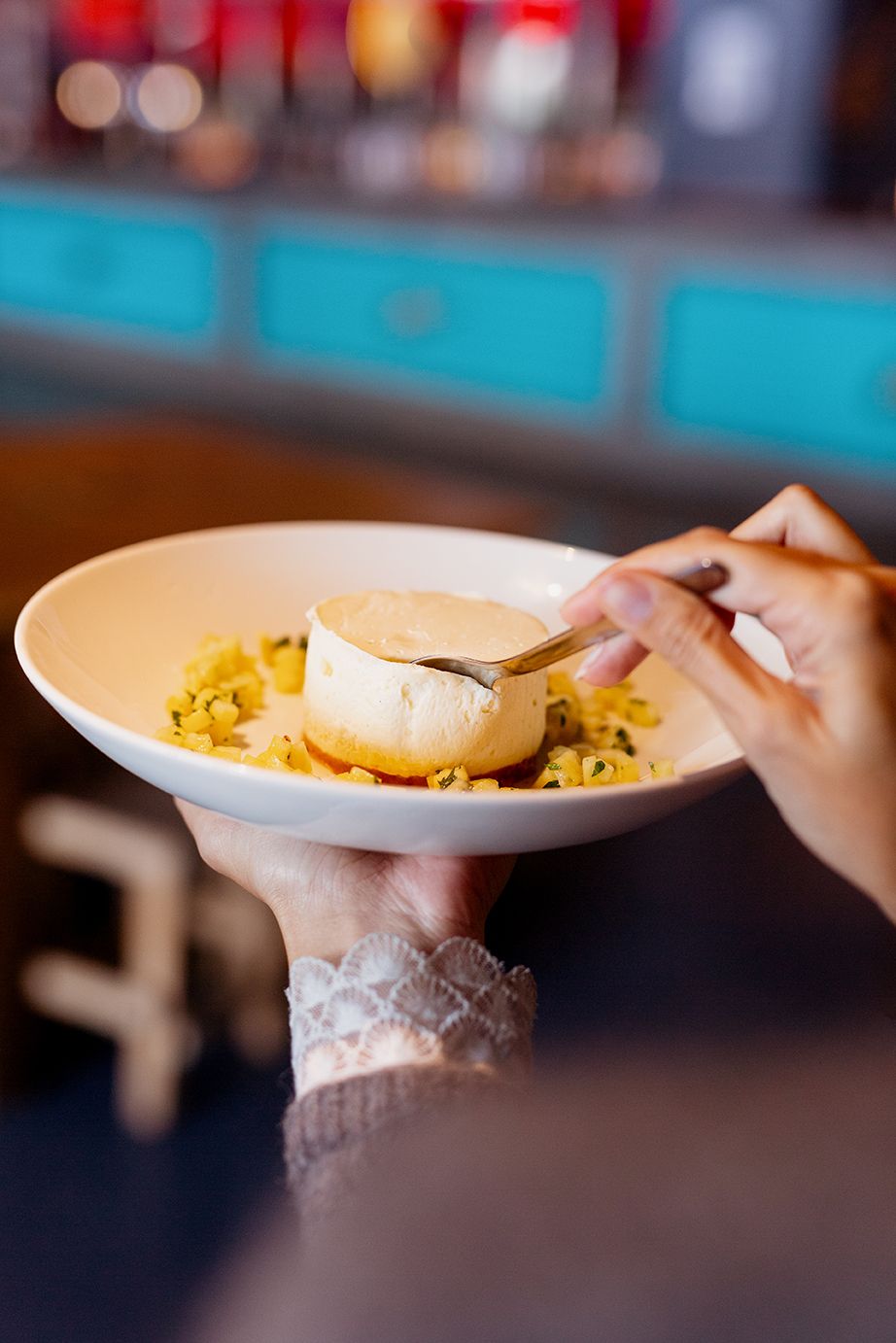 Hand holding a white bowl with a creamy dessert topped with a gold spoon.