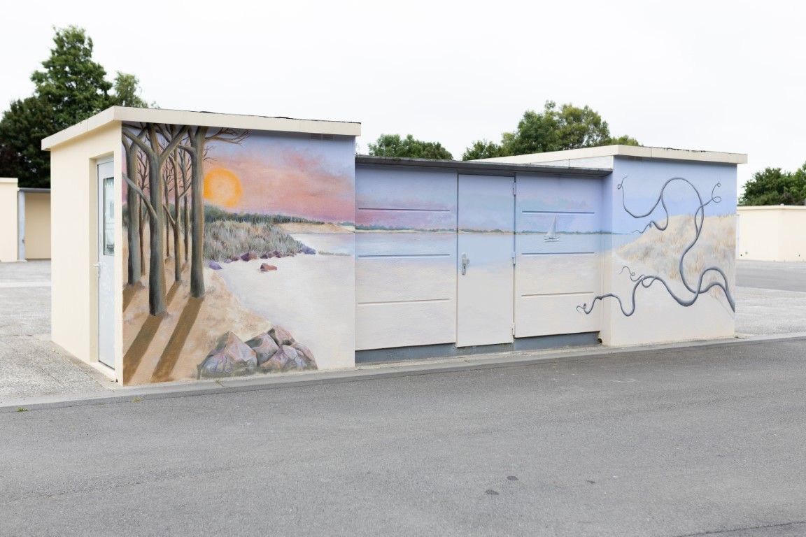 Outdoor utility buildings with colorful murals depicting a coastal landscape with trees, beach, and ocean painted on their walls.