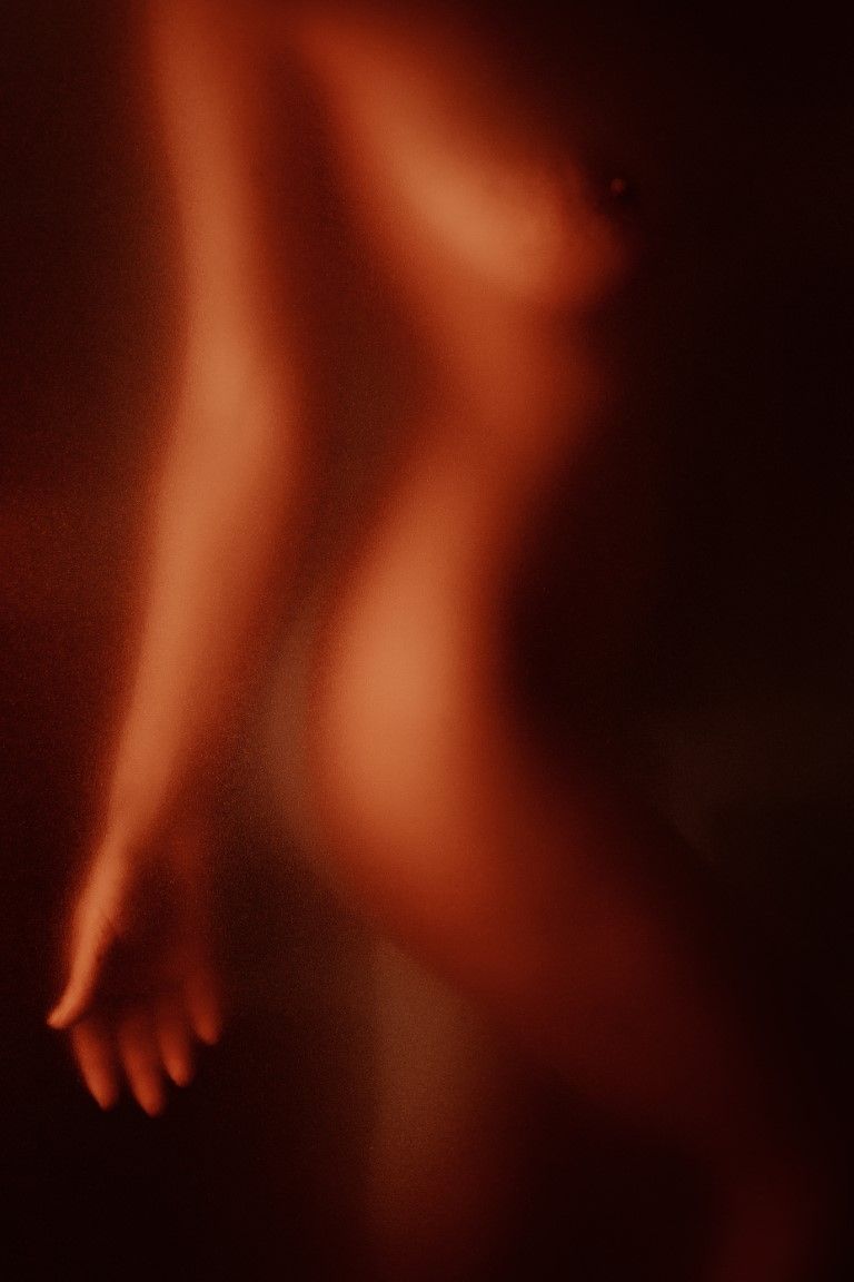 Abstract silhouette of a human figure bathed in warm red light behind frosted glass, artistic nude photography.