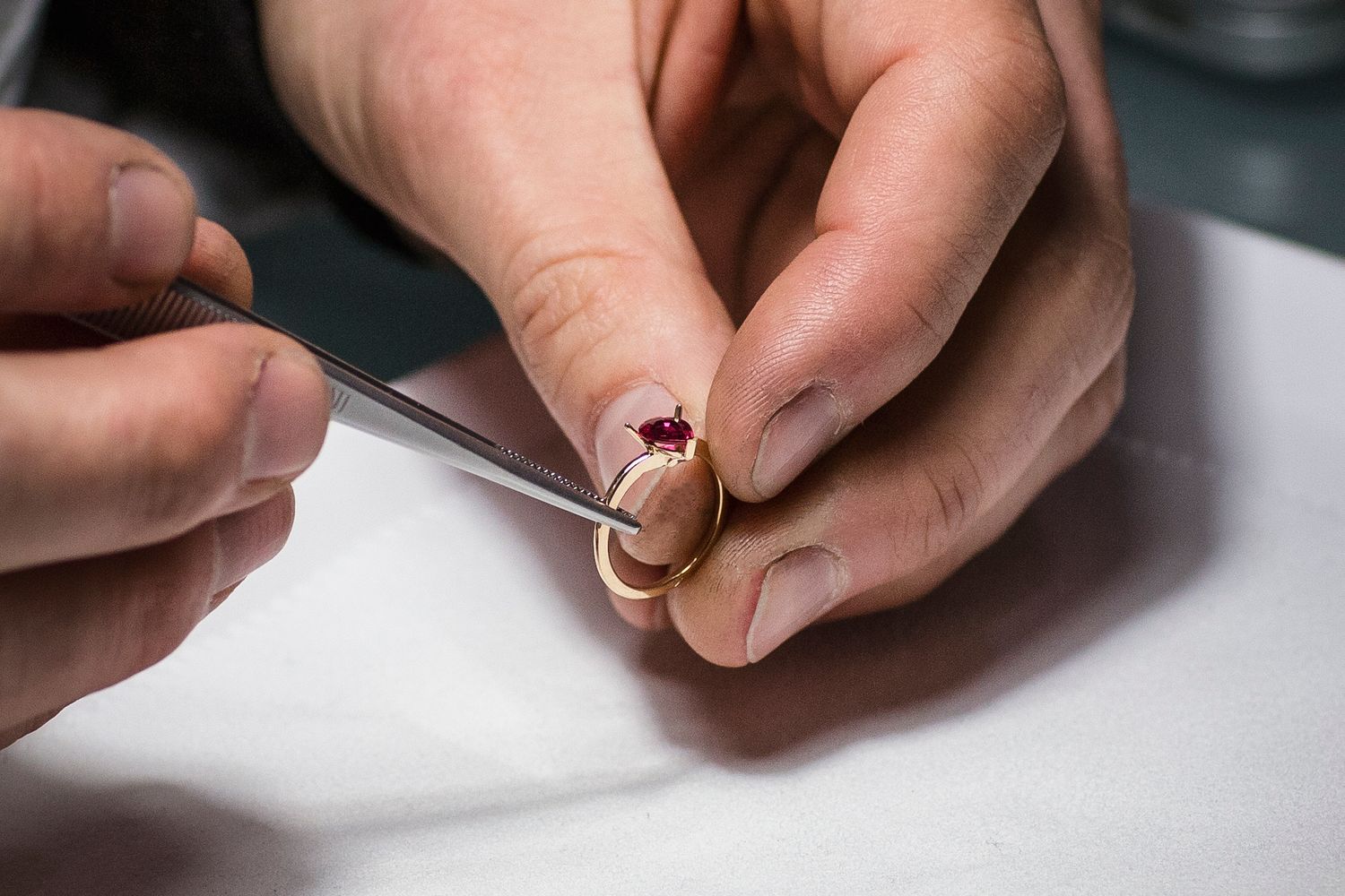 Jeweler setting a red ruby gemstone into a gold ring using precision tweezers during jewelry crafting.
