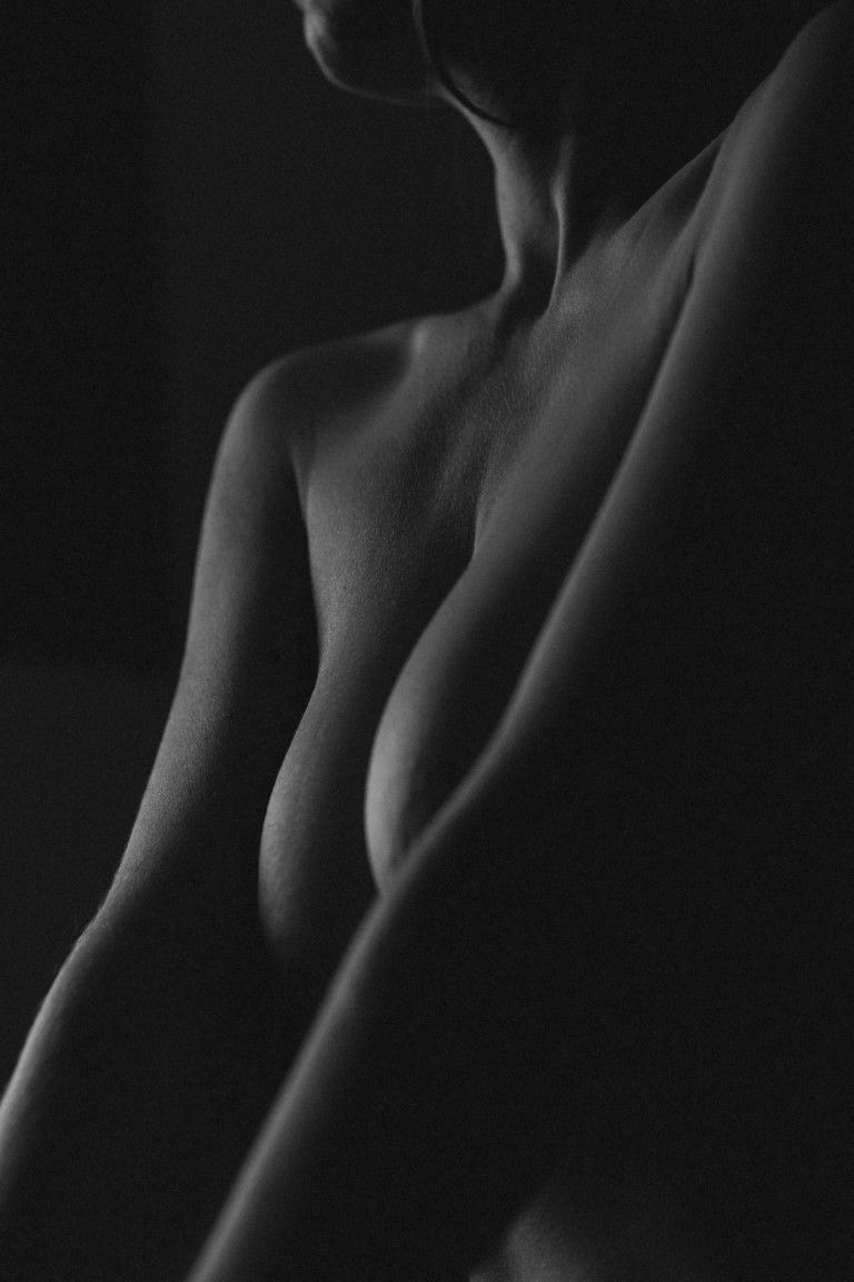 Photographie artistique en noir et blanc d'un nu mettant en valeur les courbes féminines et la poitrine dans un éclairage tamisé.