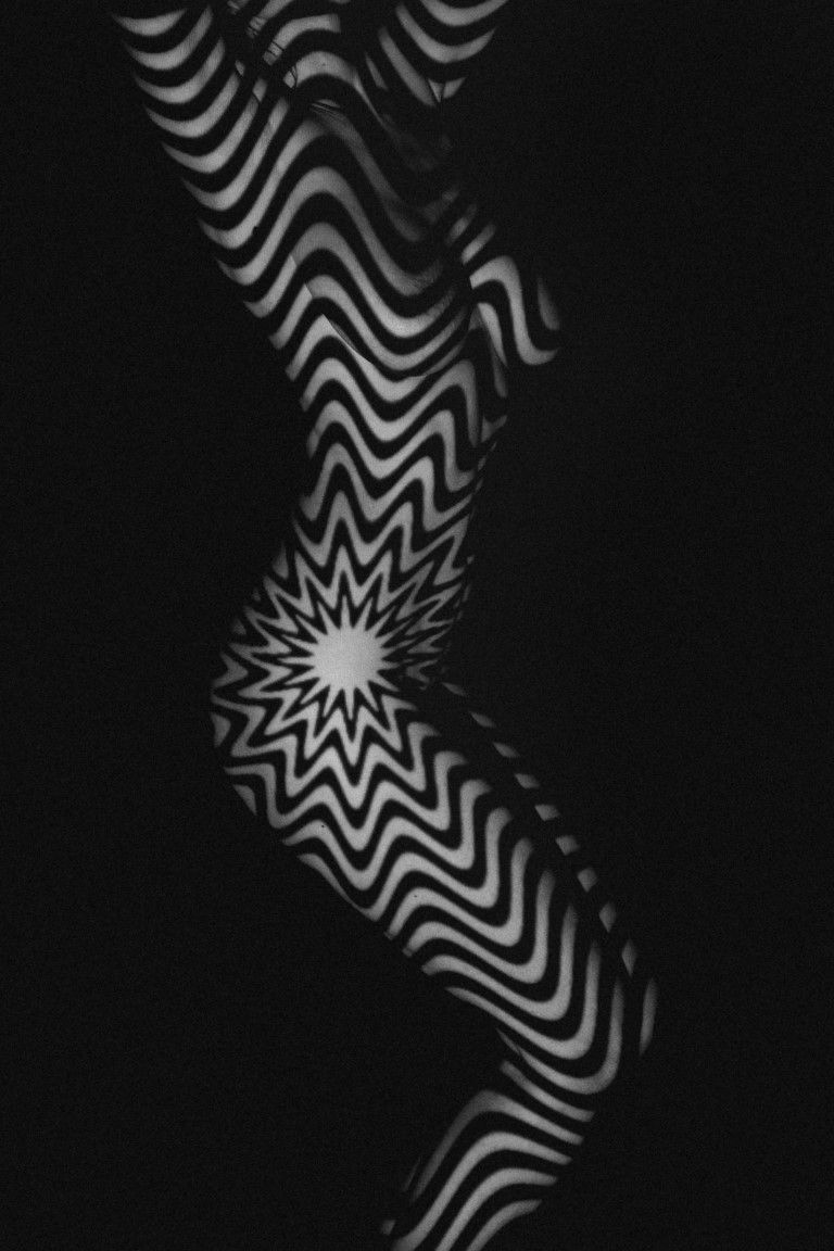 Black and white op-art pattern with hypnotic zigzag stripes forming a starburst center on dark background.