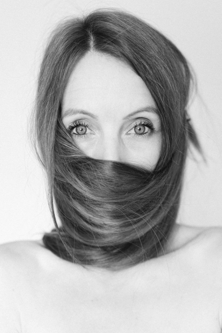 Portrait en gros plan, en noir et blanc, d'une femme aux yeux saisissants et aux longs cheveux balayés sur son visage.