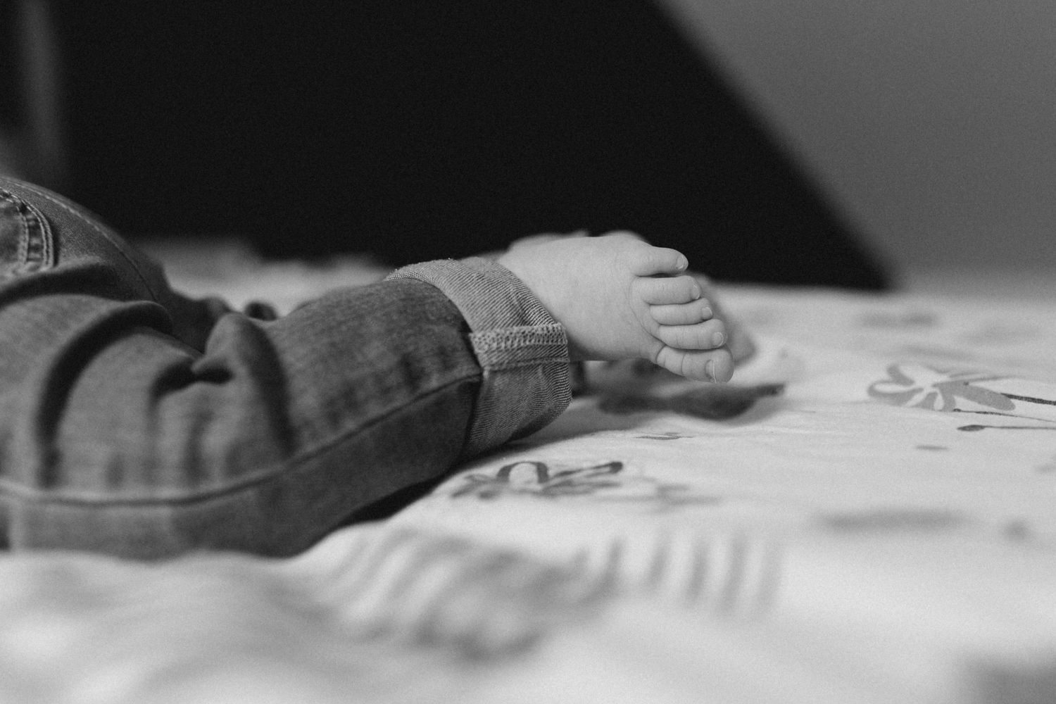 Gros plan en noir et blanc des pieds d'un bébé posés sur une couverture à motifs.
