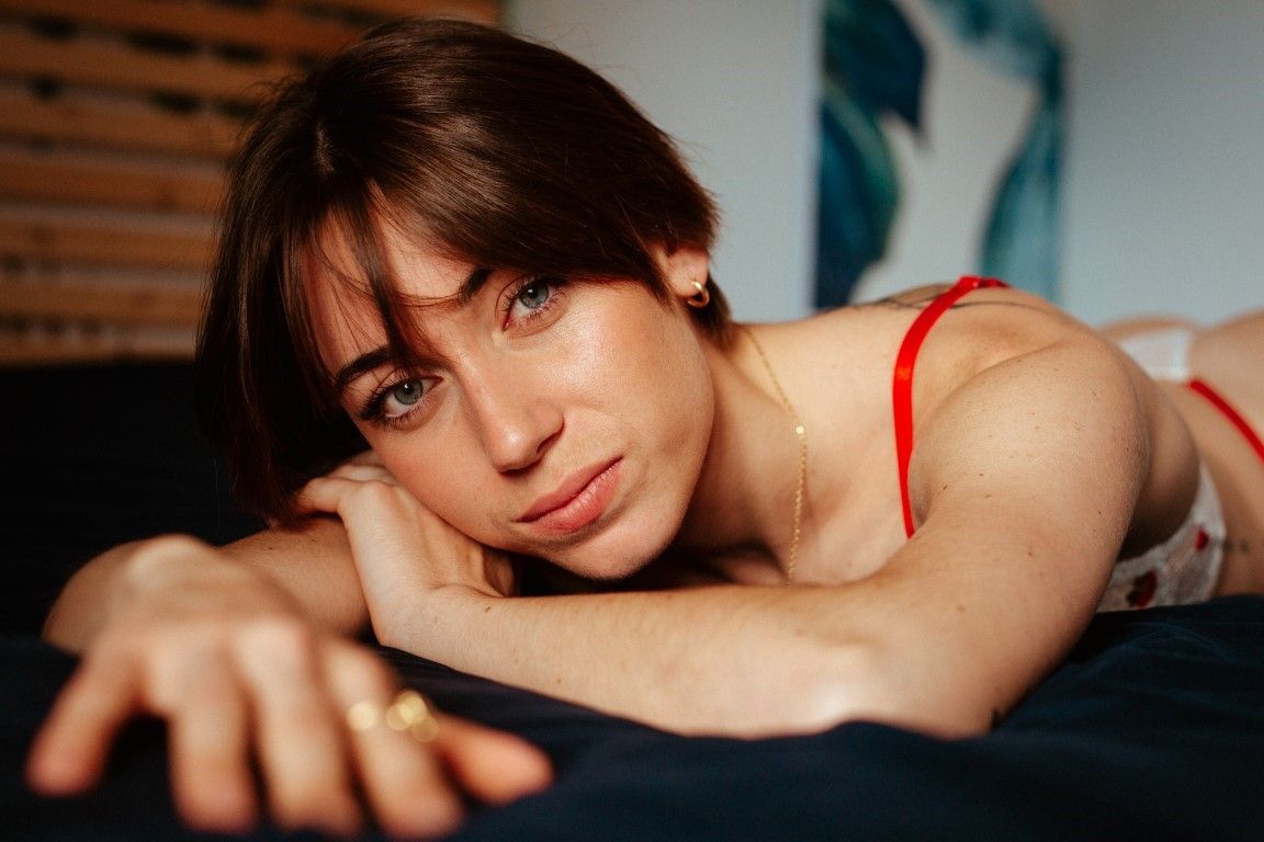Close-up portrait of a young brunette woman in red lingerie lying on a dark surface.