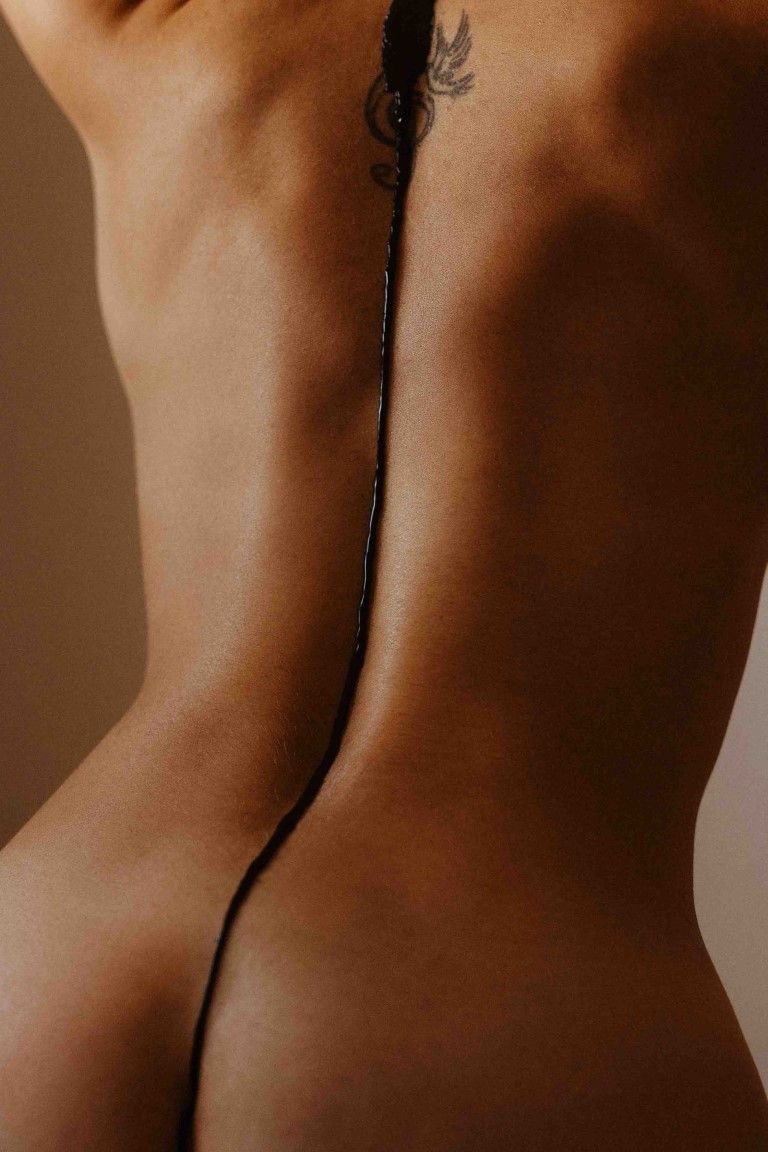 Artistic close-up of a bare back with spine tattoo and black liquid dripping down skin.