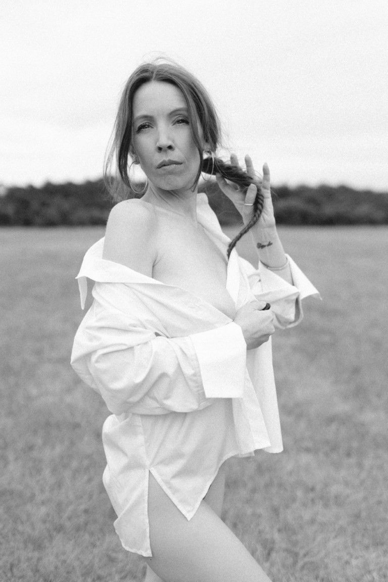 Photo en noir et blanc d'une femme en chemise blanche ouverte posant dans un champ.