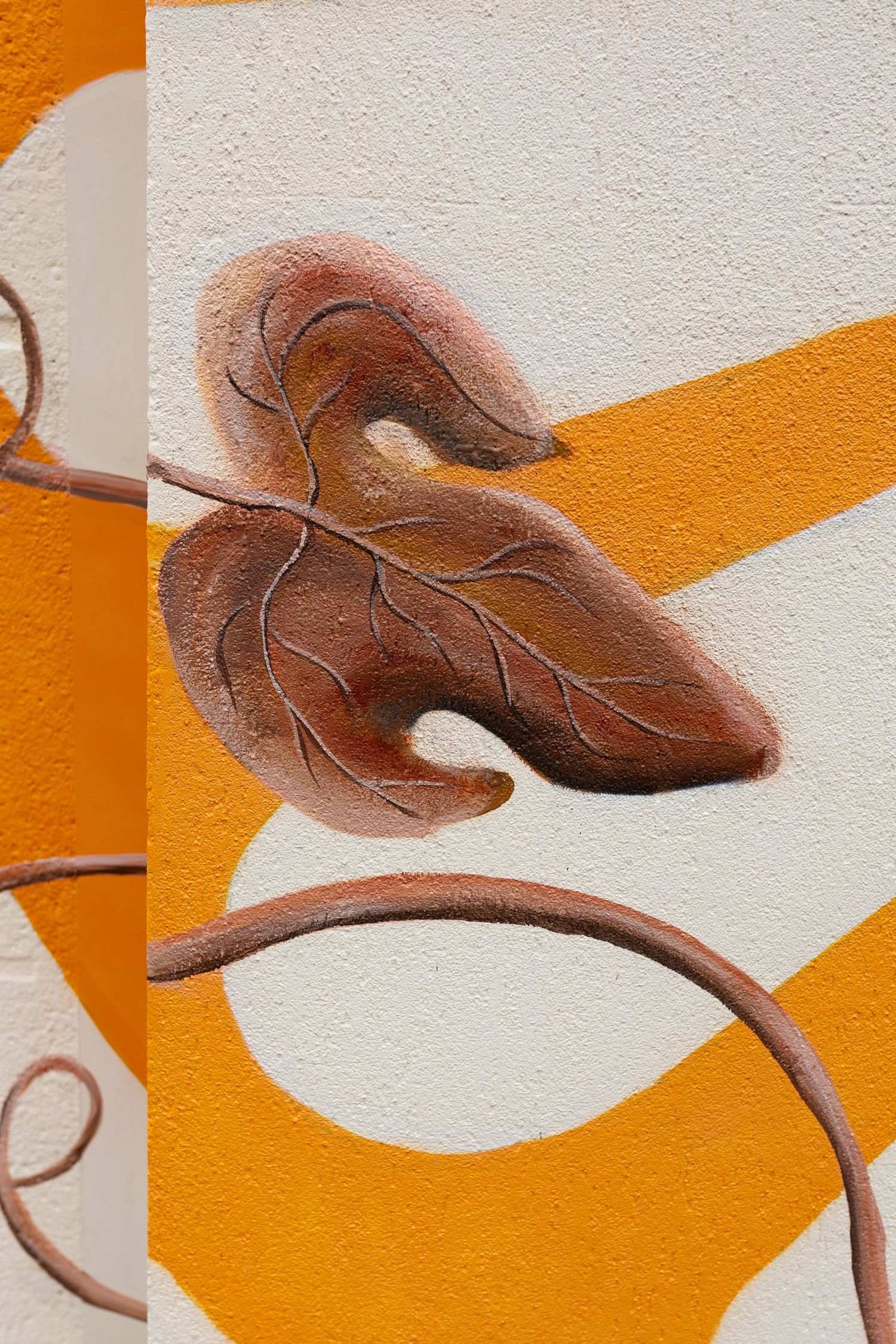 Close-up of a brown autumn leaf mural painted on a textured wall with orange and white abstract shapes.