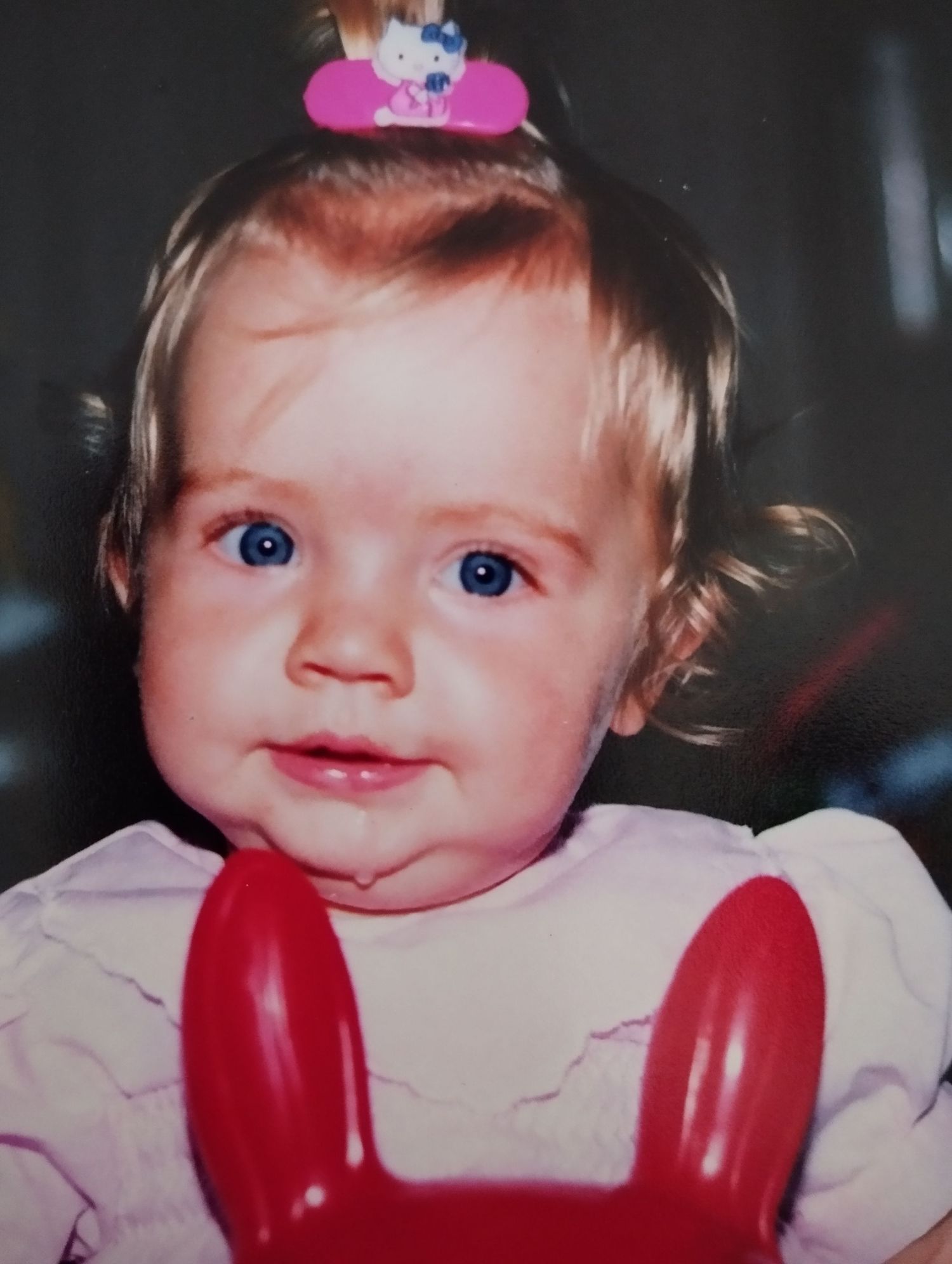 Adorable blue-eyed baby girl with Hello Kitty hair clip smiling at the camera.