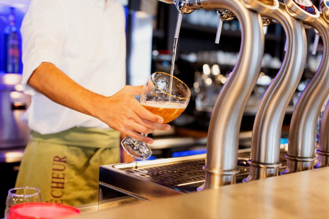 Bartender pouring craft beer from tap into a glass goblet at a bar.