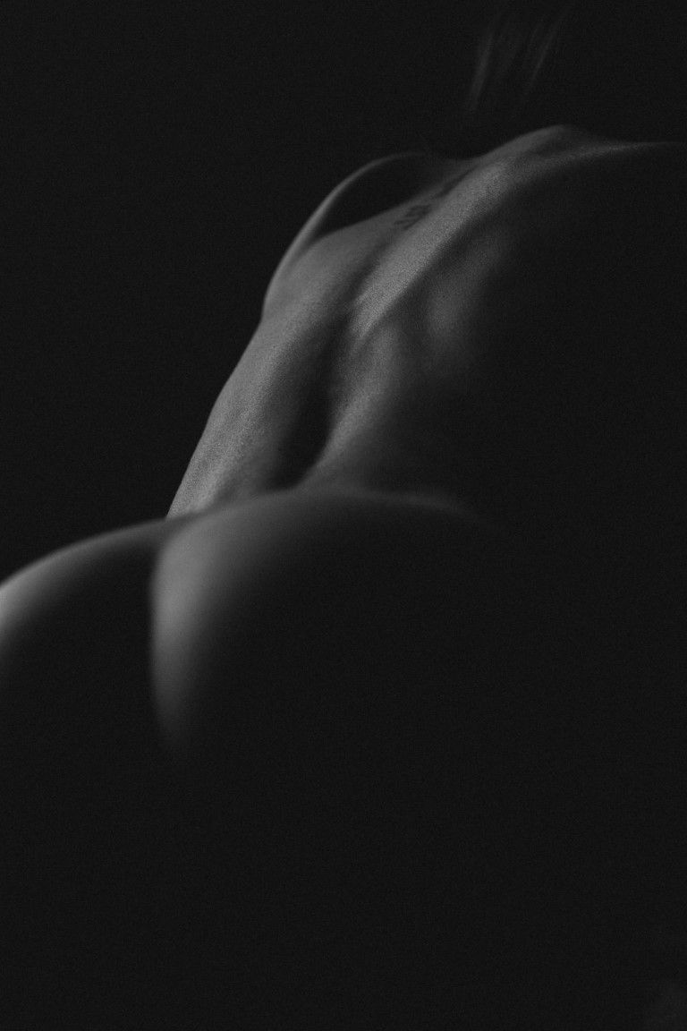 Photographie artistique en noir et blanc aux tons discrets, mettant en valeur les contours musculaires du dos et de l'épaule d'une femme.