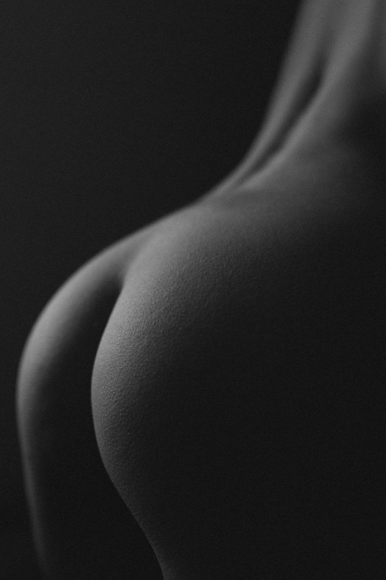 Gros plan en noir et blanc d'un nu artistique représentant le dos et les fesses d'une femme, avec un éclairage en clair-obscur dramatique.