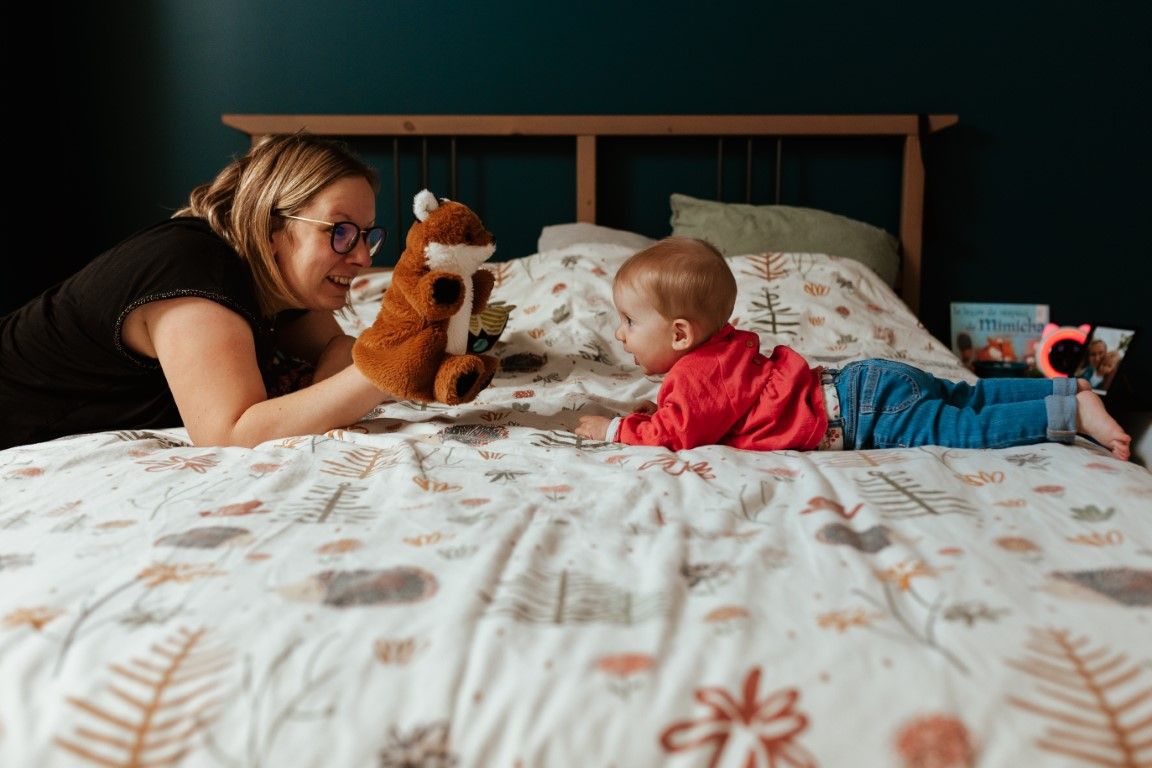 Une mère joue avec son bébé sur le lit en utilisant une peluche.