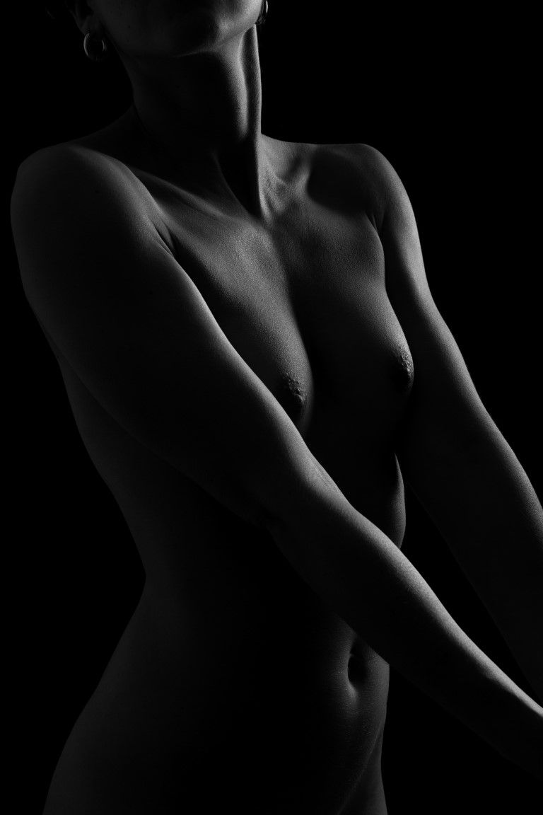 Black and white fine art nude photography showcasing elegant female form with dramatic chiaroscuro lighting.
