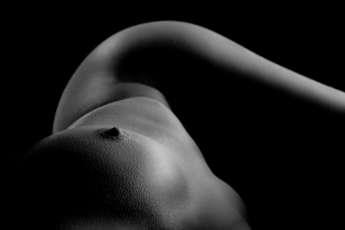 Black and white artistic nude photograph highlighting the curves of a human torso with dramatic lighting.