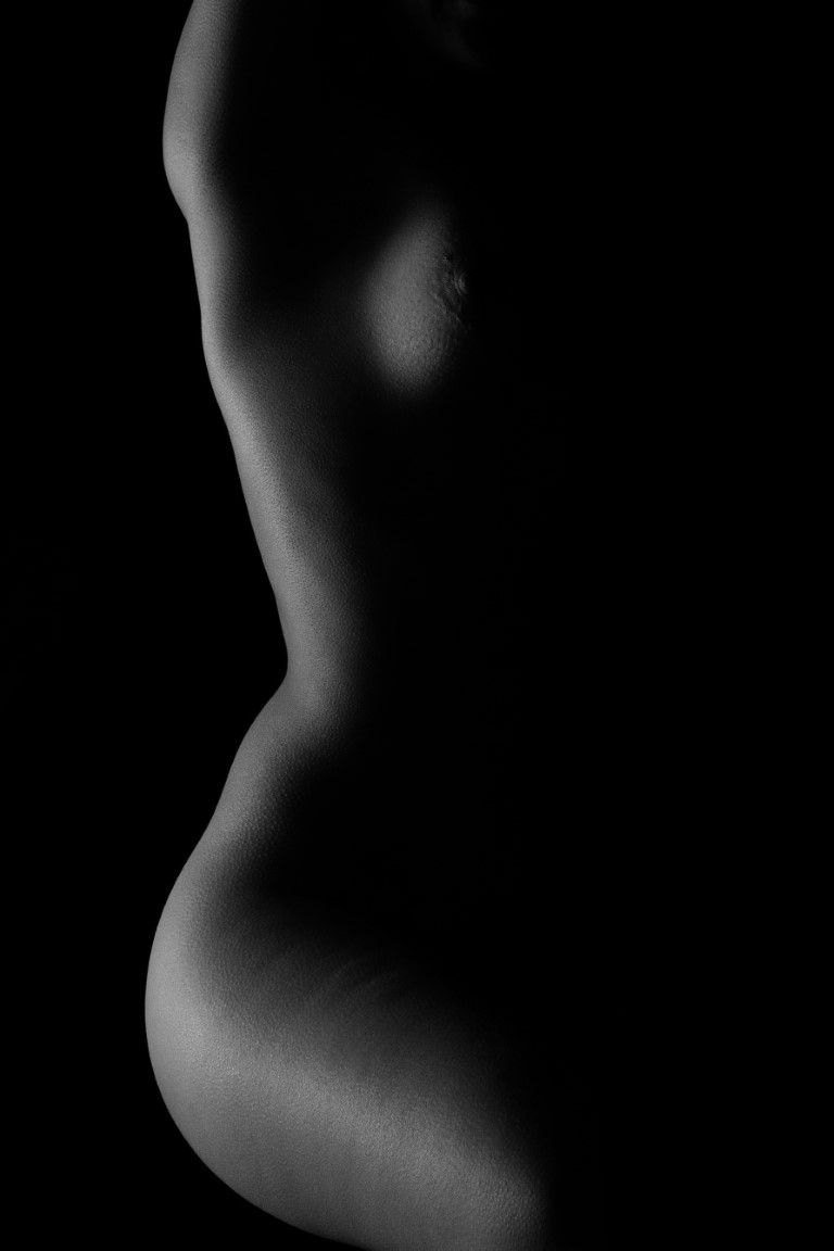 Black and white artistic nude silhouette of a woman's torso and curves against dark background.